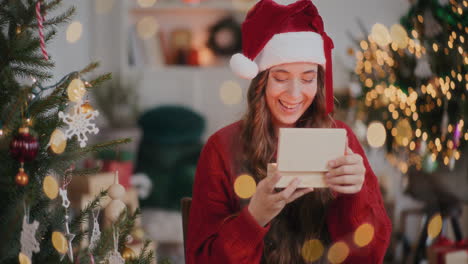 mujer asombrada en sombrero de santa abriendo una caja de regalo de madera en una casa decorada