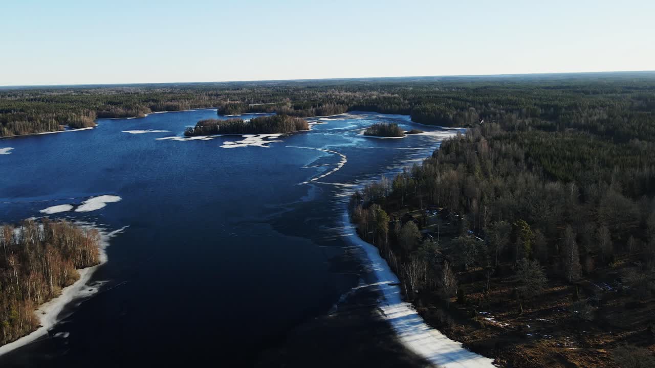 Beautiful aerial of a frozen lake surrounded by a large forest in rural Sweden on a sunny winter day