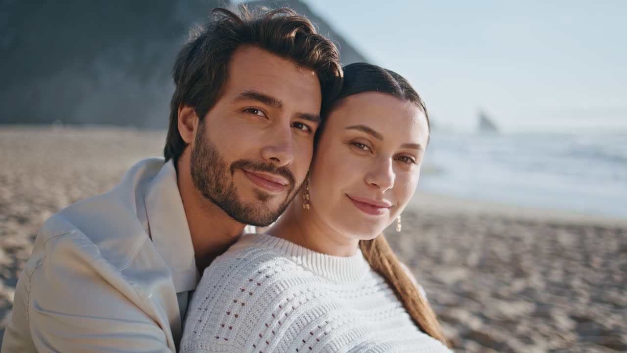 retrato de pareja romántica en la playa mirando la cámara con una sonrisa. cónyuges sentados en la costa