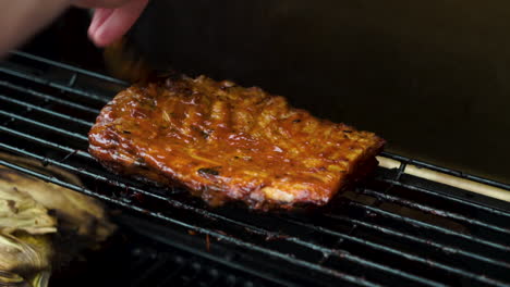 medium shot of a slow cooked pork belly being cooked on a barbecue, bbq, having miso barbecue sauce brushed on with a male hand