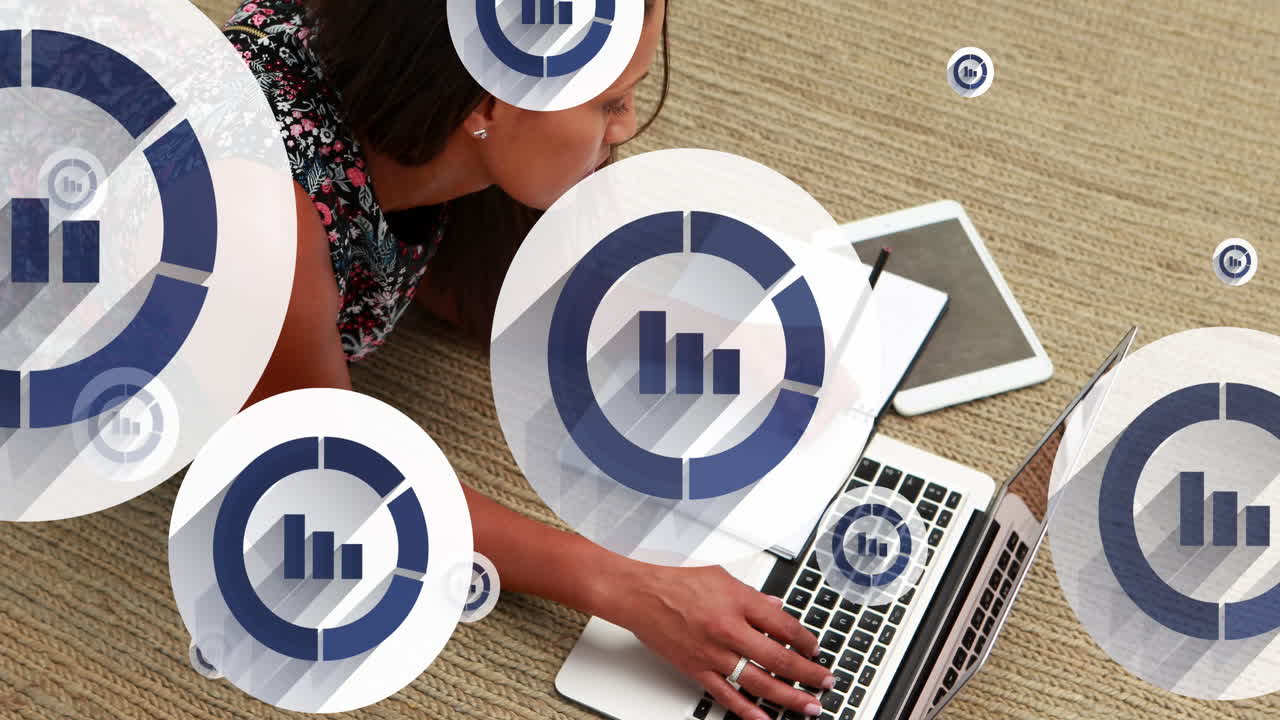 animación de iconos gráficos sobre mujer biracial acostada en el suelo con una computadora portátil y escribiendo en un bloc de notas