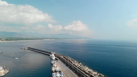 Aerial,-large-stone-ocean-breakwater-with-boats-moored-on-inside,-wide-shot