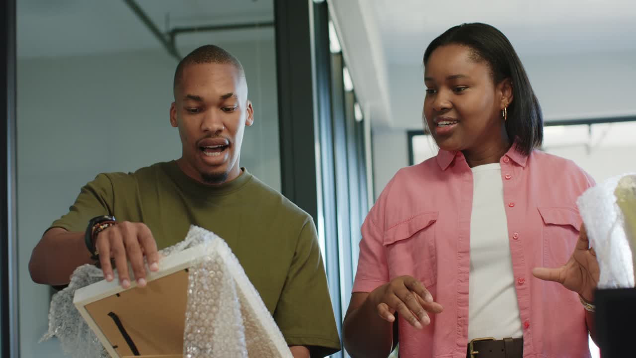 African American team woman gesturing, man peeling wrap off frame, placing for display on counter