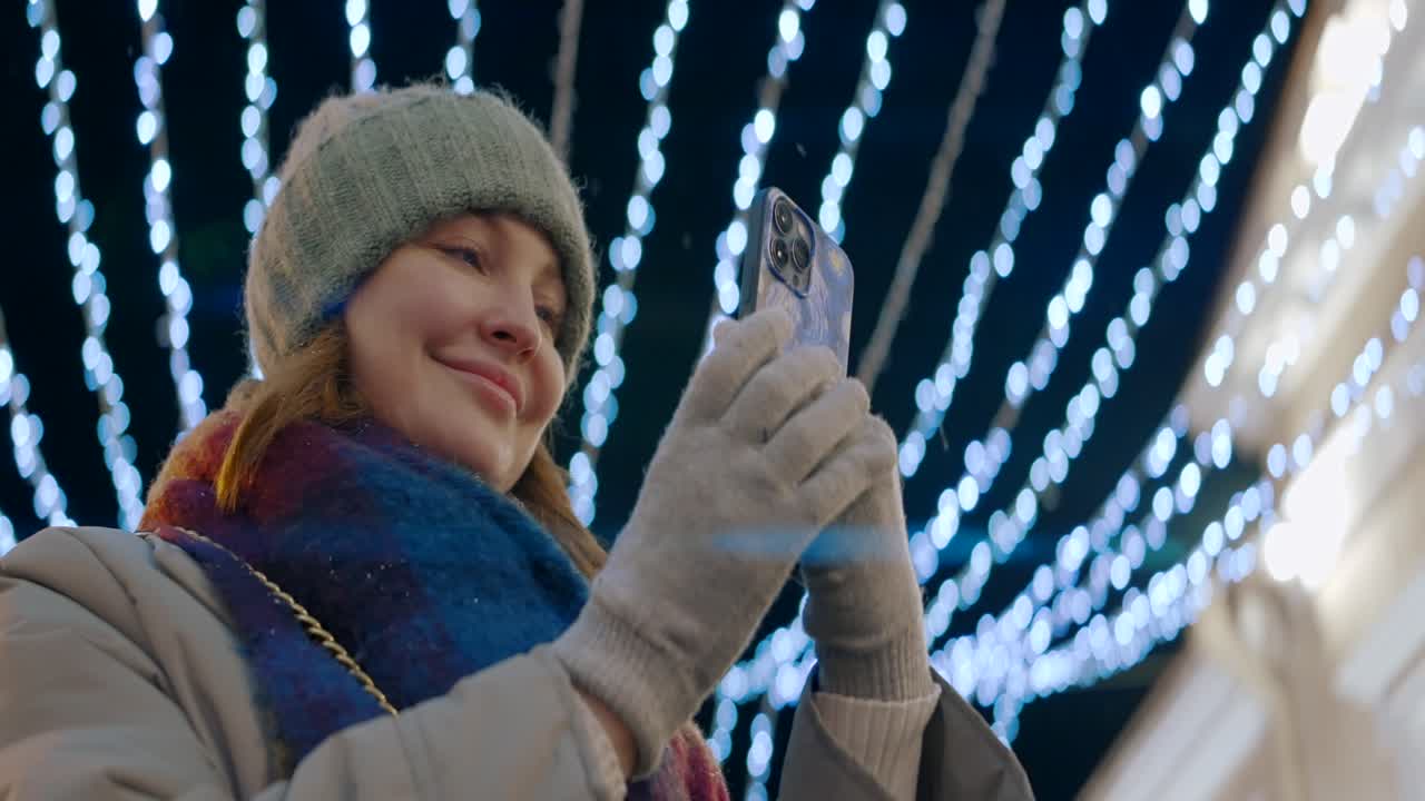 mulher usando telefone à noite com luzes de natal