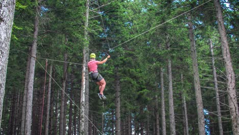 woman hanging in zip line bouncing up and down inside pine tree forest