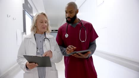 Diverse-male-and-female-doctors-in-discussion-using-tablet-in-hospital-corridor,-slow-motion