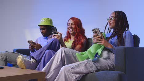 studio shot of group of young gen z friends sitting on sofa gaming and using social media on mobile phones 1