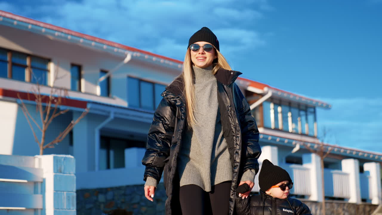 Mother and son walk in winter outdoors. Portrait of a beautiful fashionable family near the cottage house.