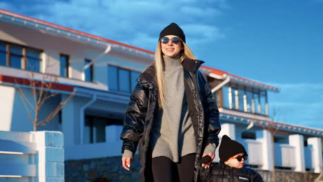 mother and son walk in winter outdoors. portrait of a beautiful fashionable family near the cottage house.