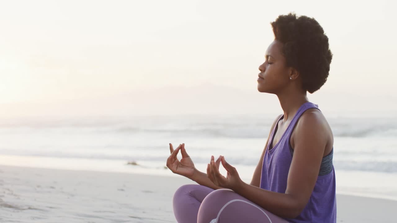 African american woman practicing yoga and meditating on sunny beach