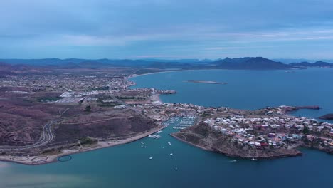 toma aérea de un dron sobre el mar hacia un puerto deportivo con un día soleado a gran altura y vistas al océano