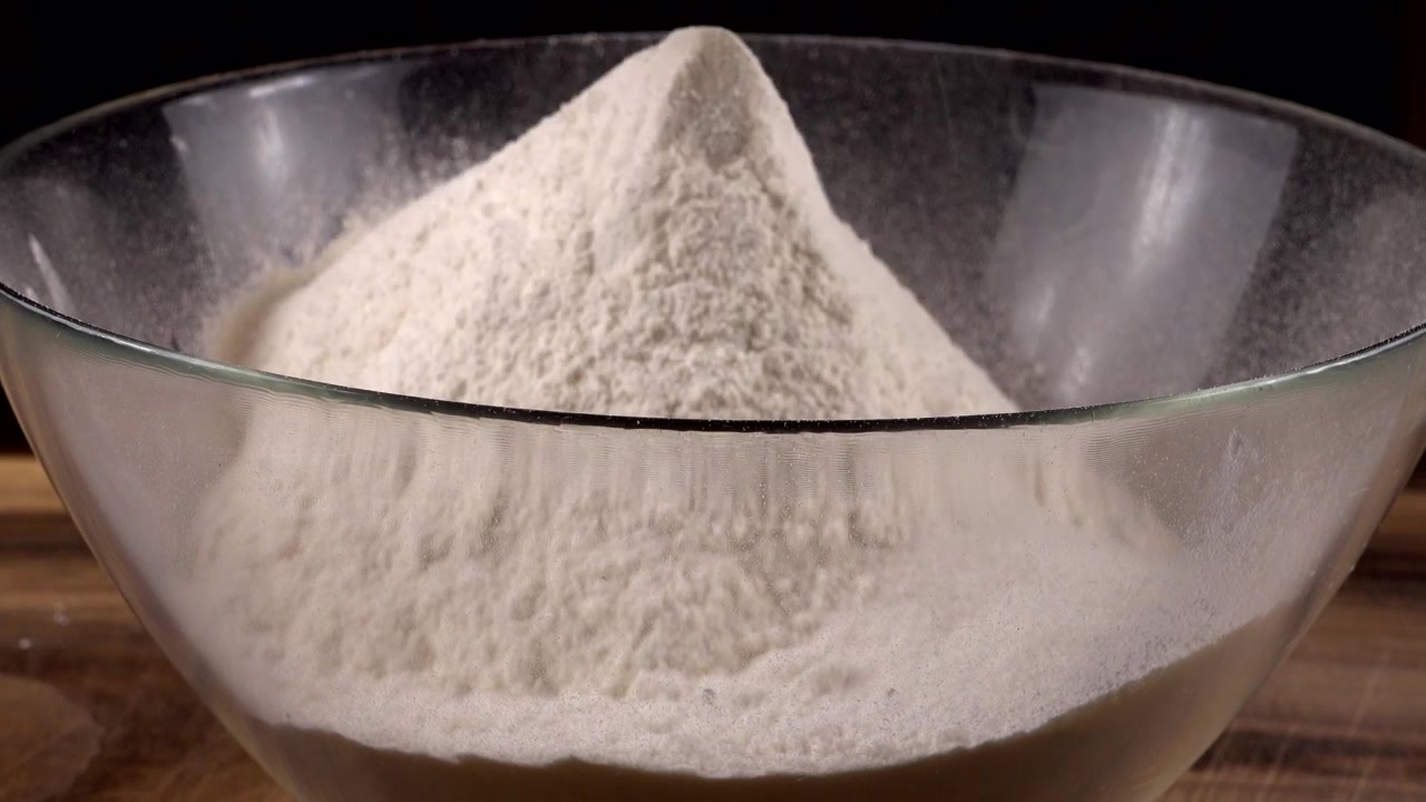 Mengayak tepung menggunakan saringan ke dalam mangkuk kaca di dapur.