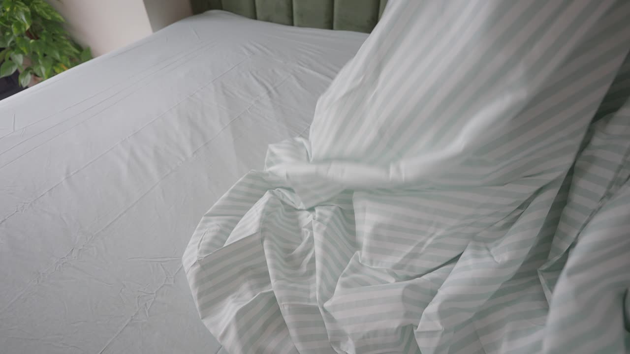 Close up of a bed with a striped sheet and a person's hand