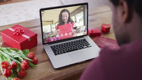 Glückliche-Biraziale-Frau-Mit-Vitiligo,-Die-Ein-Geschenk-öffnet-Und-Einen-Valentinstag-Videoanruf-Auf-Dem-Laptop-Macht