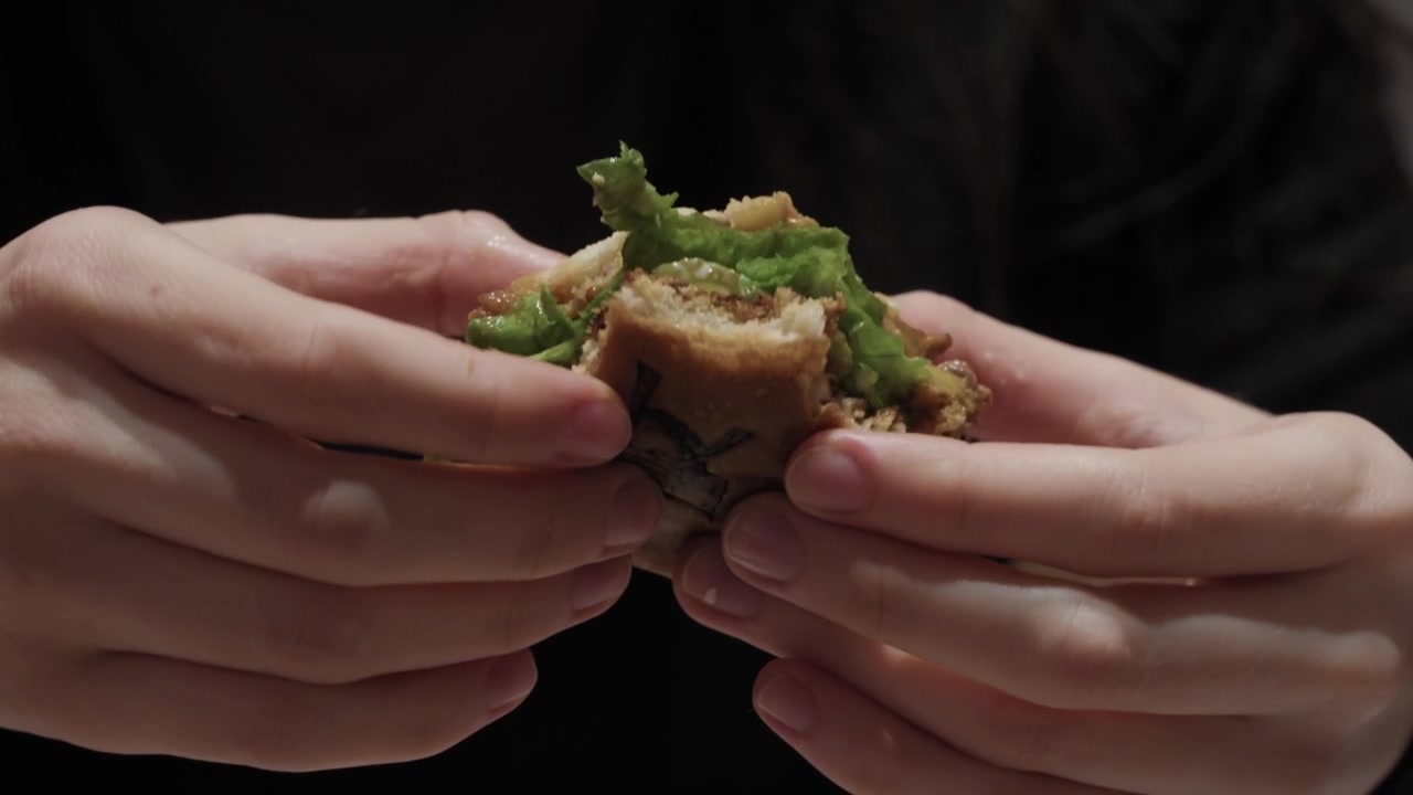 Two hands holding bitten burger with green sauce visible inside bun
