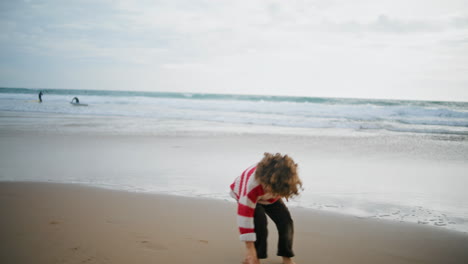 kid playing autumn beach with parent on cloudy day. barefoot curly boy resting