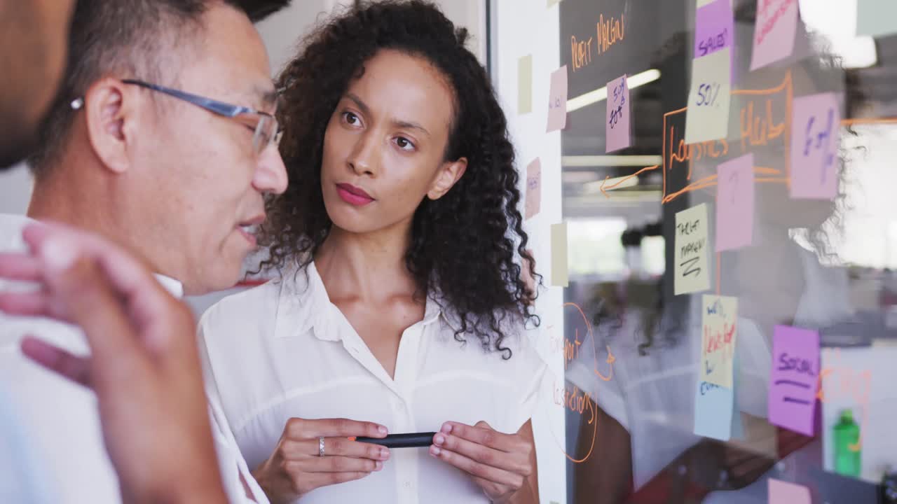 hombre de negocios sénior discutiendo con jóvenes empresarios sobre notas de memorando en tablero de vidrio