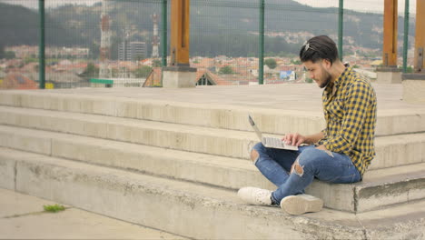 Handsome-guy-sitting-on-stairs-working-on-his-laptop-and-cellphone