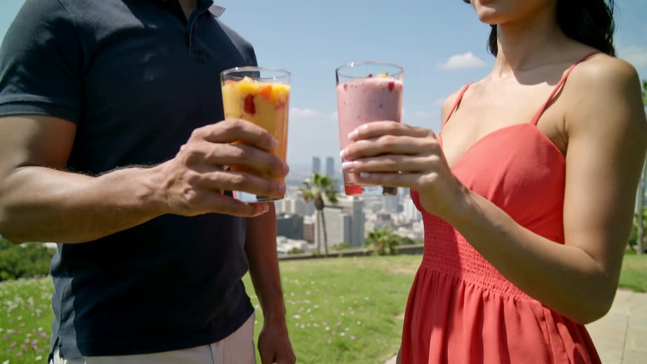Erkek ve kadın smoothie'leri tokuşturuyor, kamera geri çekiliyor ve reklam için şehir silüeti kadraja alınıyor.