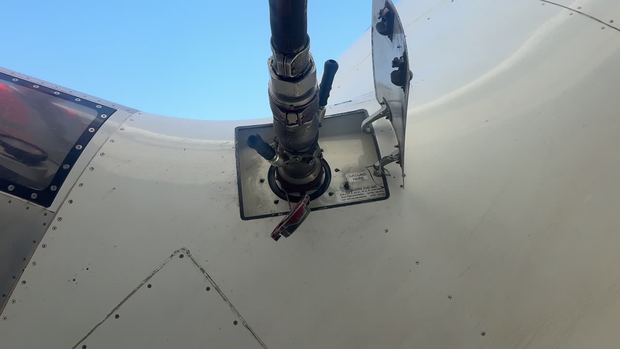 Close-up view of the refuelling process of a white color fuselage jet at the parking stand, with a view of the hose connected. Low angle view shot