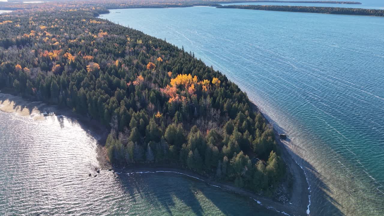 Aerial view of a forested peninsula surrounded by clear blue water with vivid fall foliage and soft morning light
