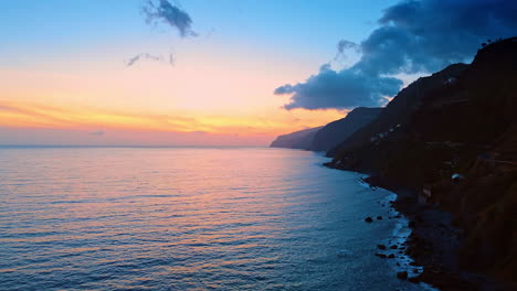 dark rocks of the madeira islands meet the waves of the north atlantic ocean. beautiful pink sky at sunset over the horizon.