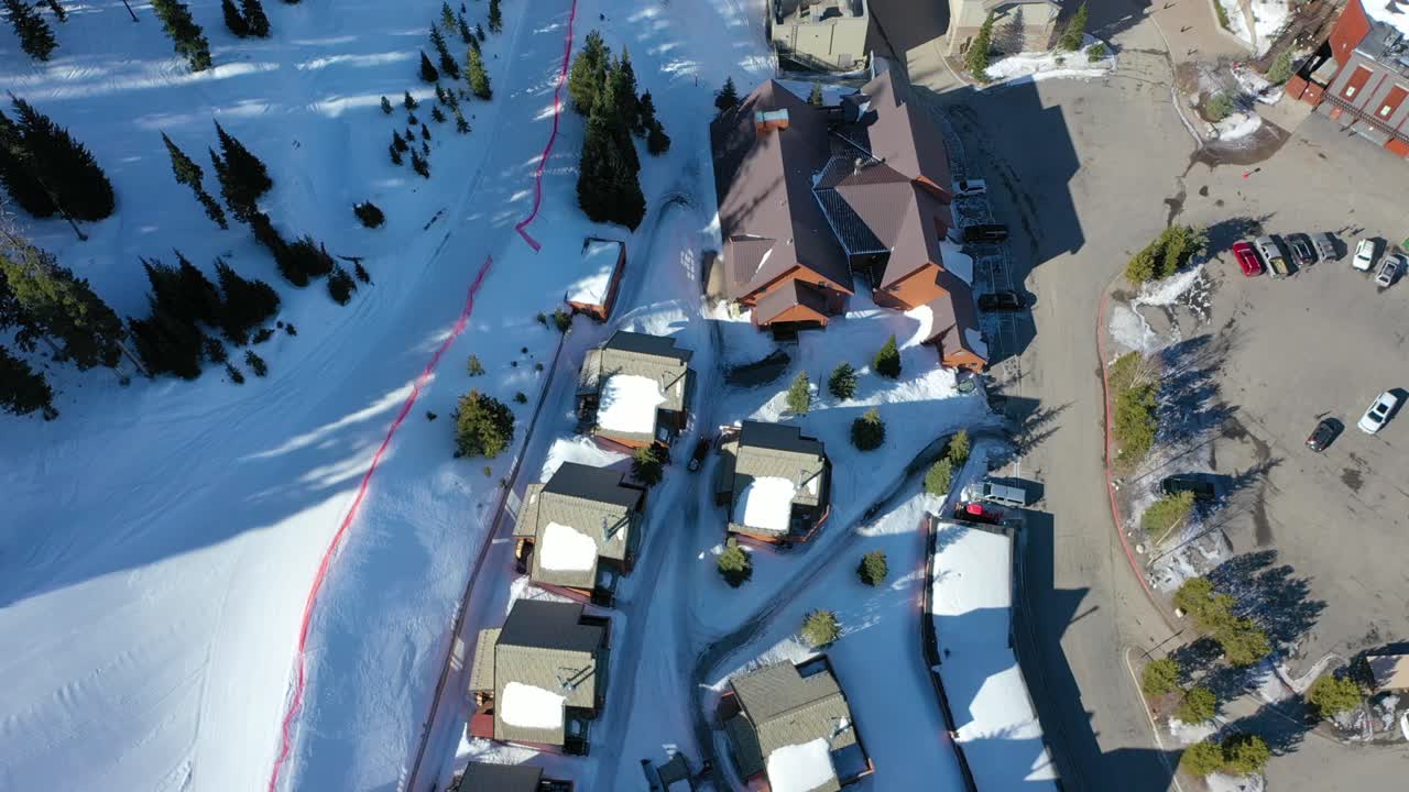 Drone captures snowy mountain condos from above in Big Sky Montana, nestled in evergreens, with ski slopes and white peaks creating the perfect alpine vacation escape