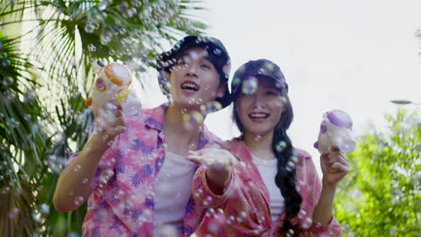 couple in love making soap bubble in front of camera with palm tree on background , summer tropical vibes