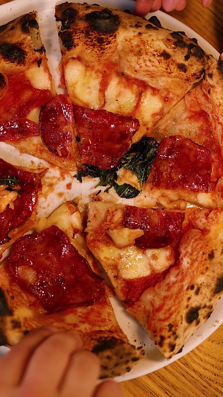 Vista dall'alto di persone che prendono fette di pizza fresca al salame piccante da un piatto bianco.