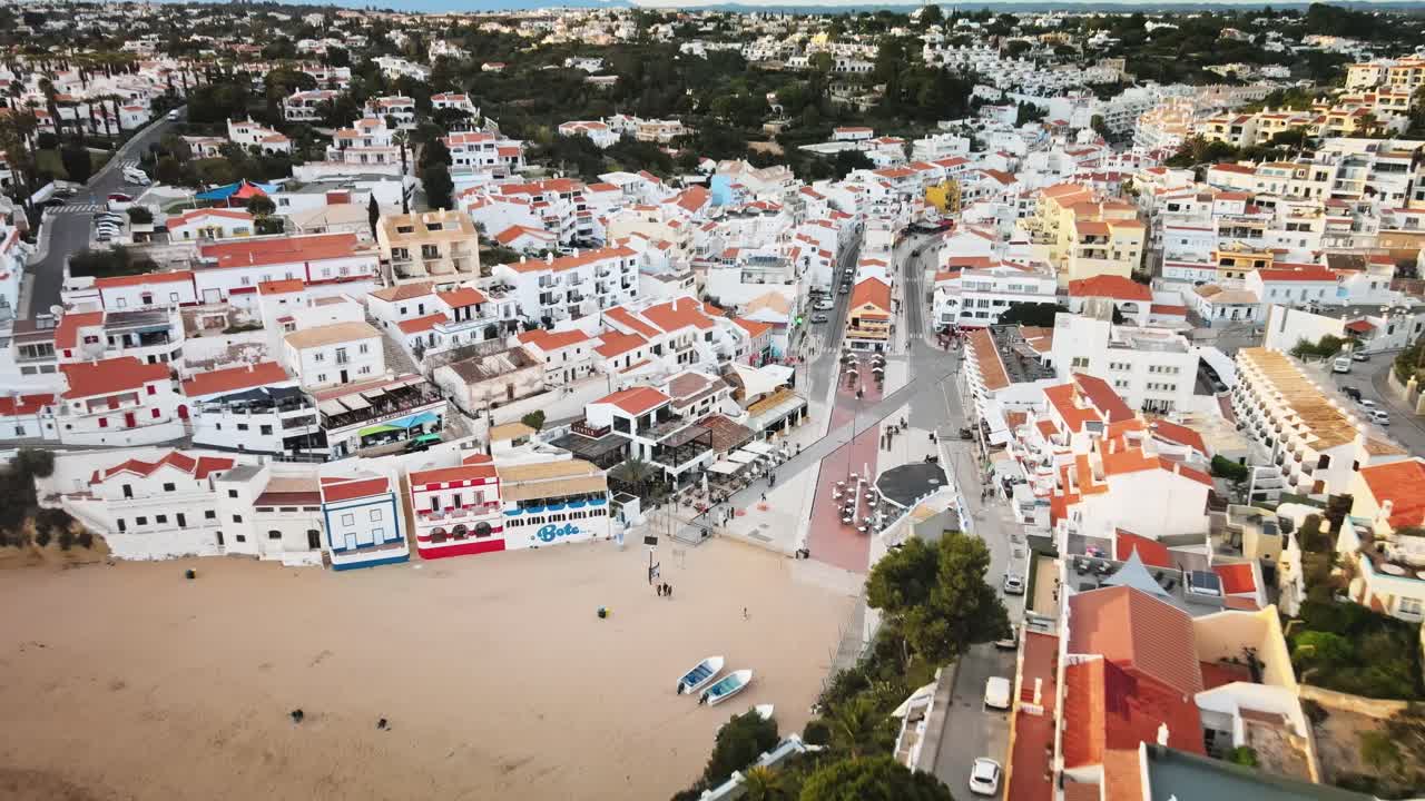 Camera pushes forward and descends from clifftop roads toward golden beach, whitewashed buildings, and red-tiled roofs nestled in the lush Algarve landscape