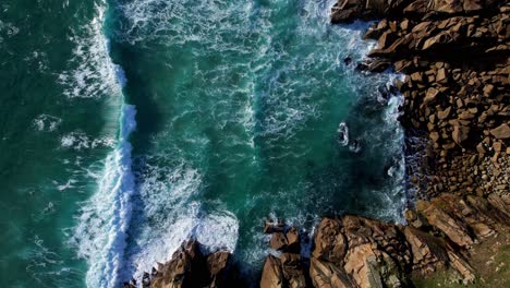 green ocean waves along rocky cornish coastline, aerial top down panning shot