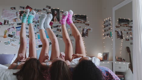 happy teen girls lying on bed at home with legs up having fun wiggling feet hanging out wearing pajamas enjoying relaxing morning on weekend