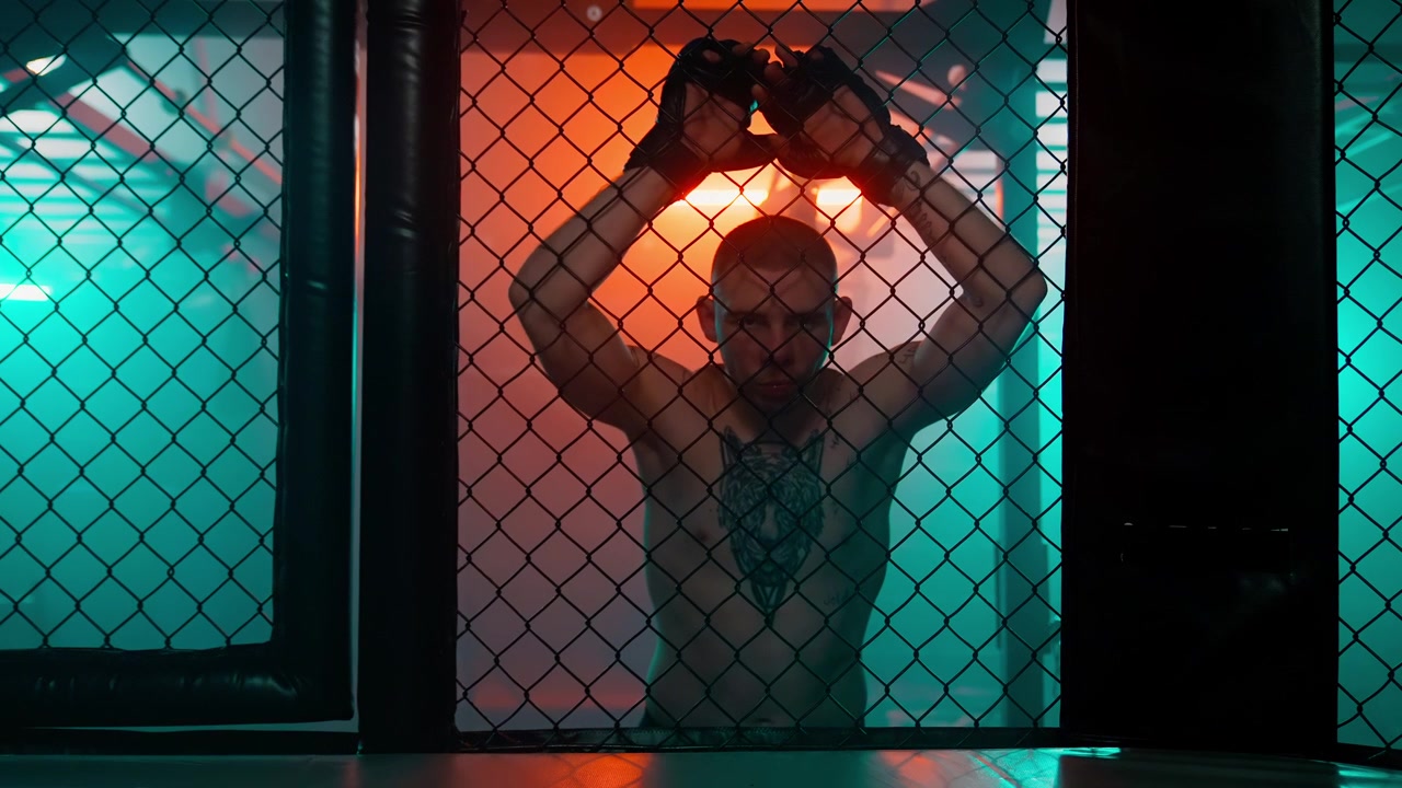 Męski zawodnik MMA pozujący w klatce z dramatycznym oświetleniem