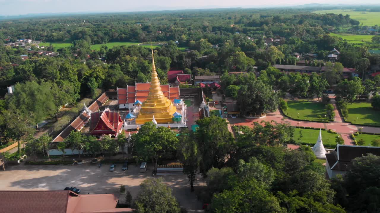 4K luftdroneoptagelse - Thailandsk buddhistisk tempel på en solrig dag, gylden pagode omgivet af grønne træer, rødt tag, thailandsk kultur, religiøs tro og meditation, historisk sted, kameraet glider til venstre