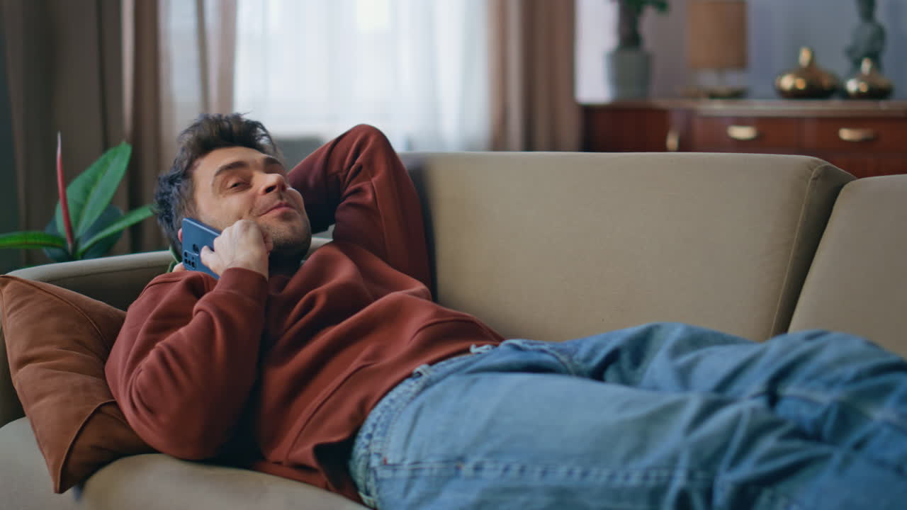 Chilling guy calling smartphone lying on home sofa close up. Smiling man talking