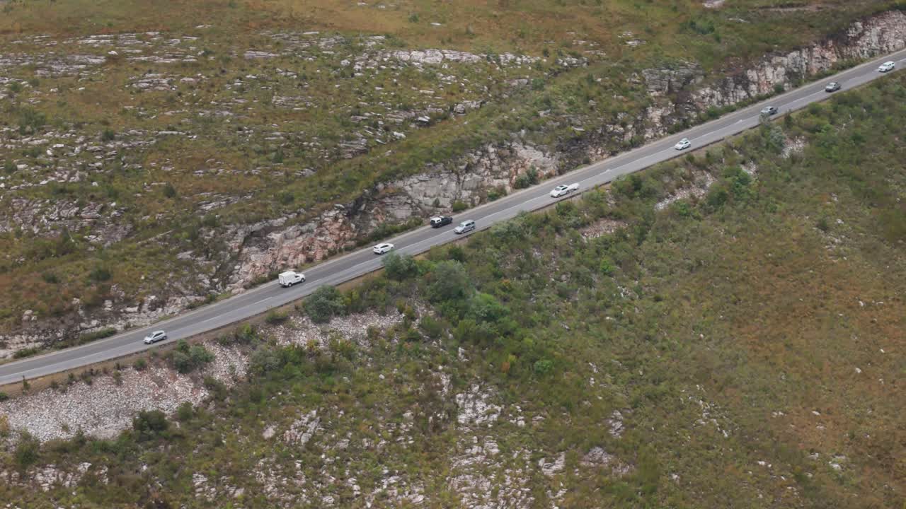 воздушный снимок, следующий за автомобилями на извилистой горной дороге в западном кейпе, южная африка, захватывая момент, когда одна машина обгоняет другую, демонстрируя живописную поездку по неровной местности.