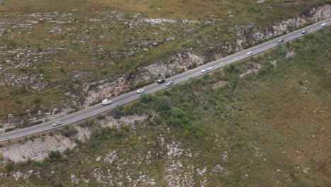 fotografía aérea siguiendo a los coches en una sinuosa carretera de montaña en el cabo occidental, sudáfrica, capturando el momento en que un coche supera a otro, mostrando el recorrido panorámico a través de un terreno accidentado.