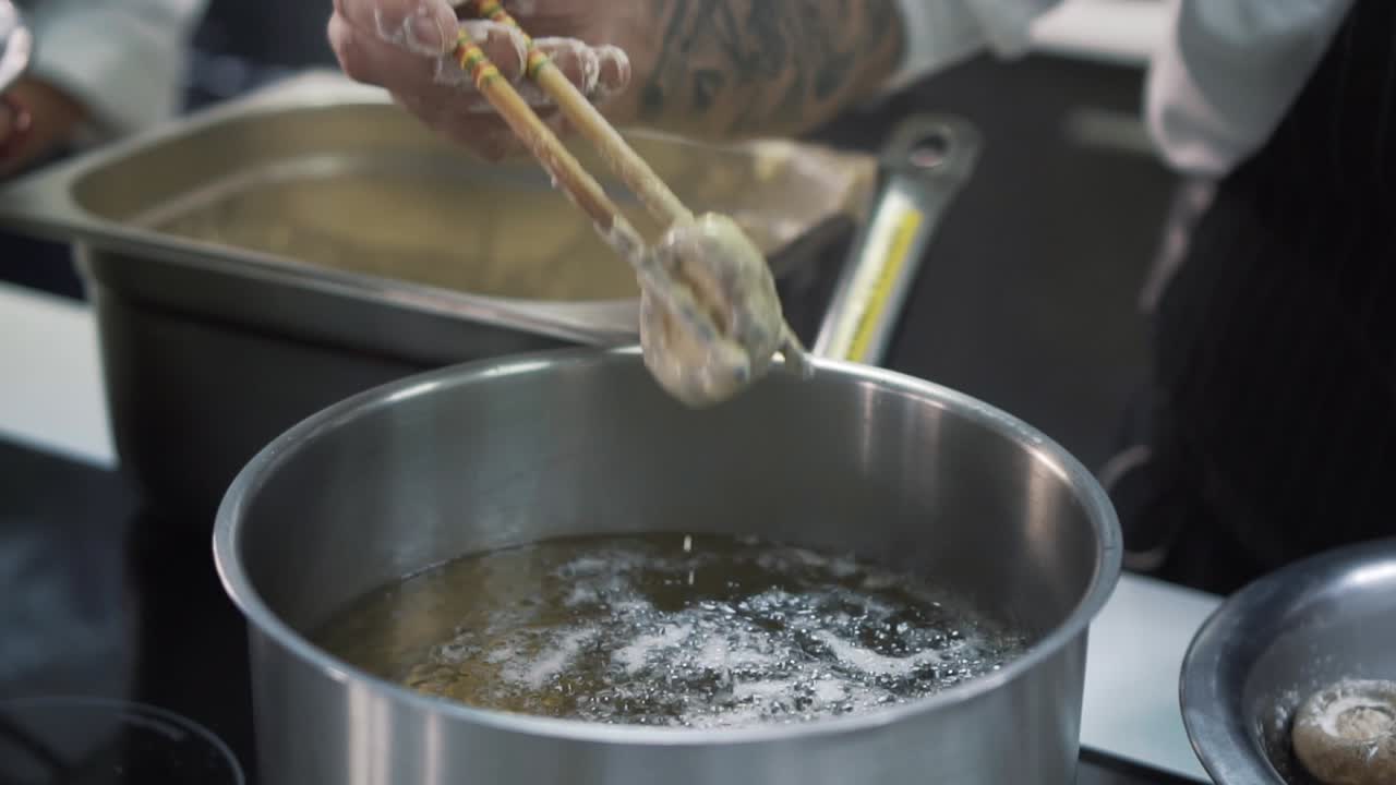 Professional chef dipping freshly made mushrooms into hot oil for cooking