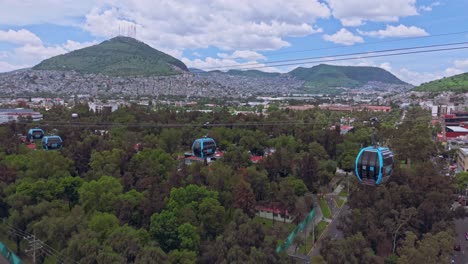 Aerial shot of cable cars on a cable system above greenery with mountains in the background