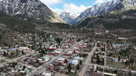 Luftaufnahme,-Langsames-Schwenken-über-Eine-Kleine-Stadt-Mit-Großen-Schneebedeckten-Bergen-Im-Hintergrund,-Mit-Blauem-Himmel-Und-Wolken,-Spätfrühling-In-Ouray,-Colorado