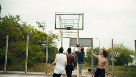 a man in a gray t-shirt dribbles in basketball and scores a brilliant goal for his team. he is very happy about his success and is supported by his team on the outdoor basketball field