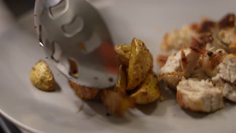 close up of loading greek potato wedges onto plate with spoon, slow motion