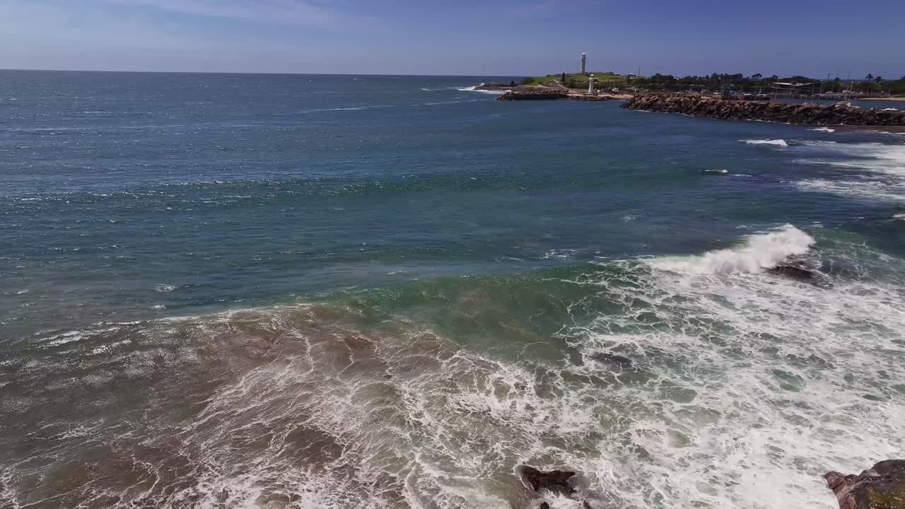 aérea que se eleva sobre las rocas y las olas y revela los faros y el puerto de wollongong más allá