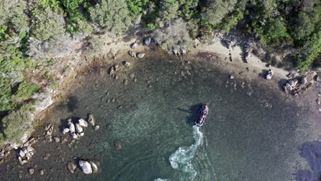 Aerial-view-of-a-small-boat-approaching-a-rocky-shore-surrounded-by-lush-greenery