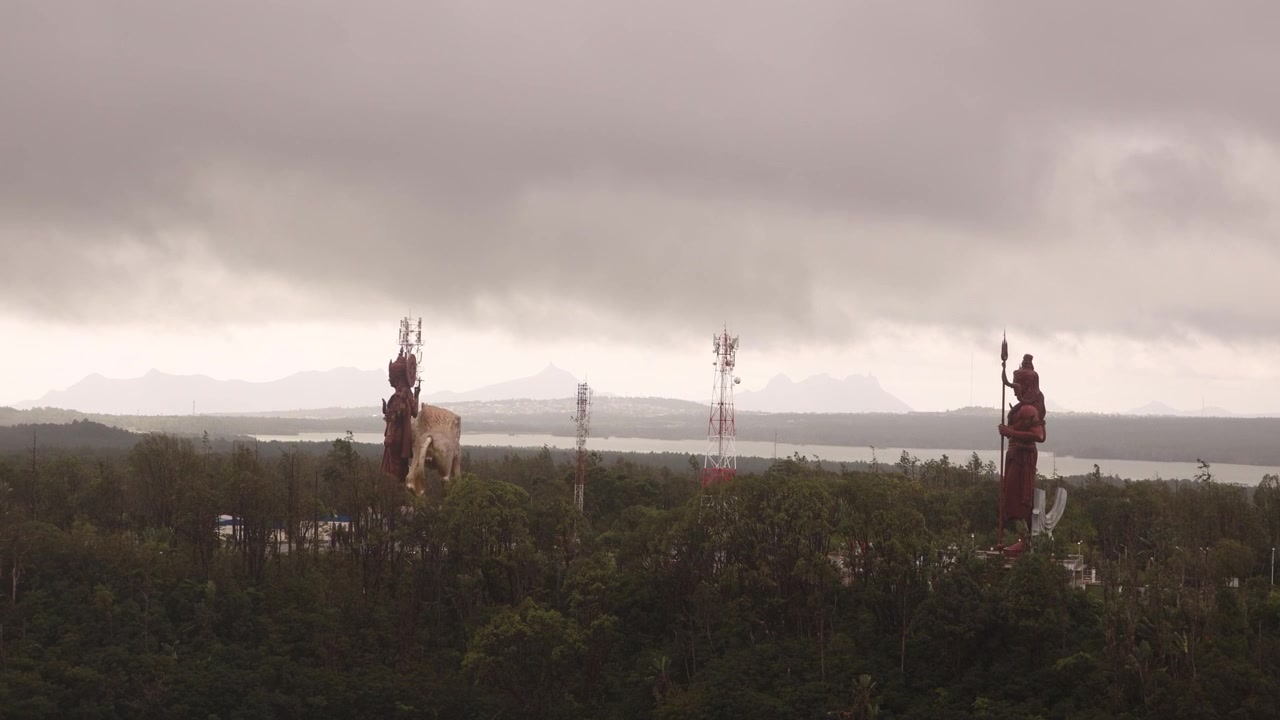 Cloudy aerial view of the sacred Ganga Talao, or Grand Bassin, featuring the colossal Hindu deity statues overlooking the holy crater lake in the mountainous heart of Mauritius.