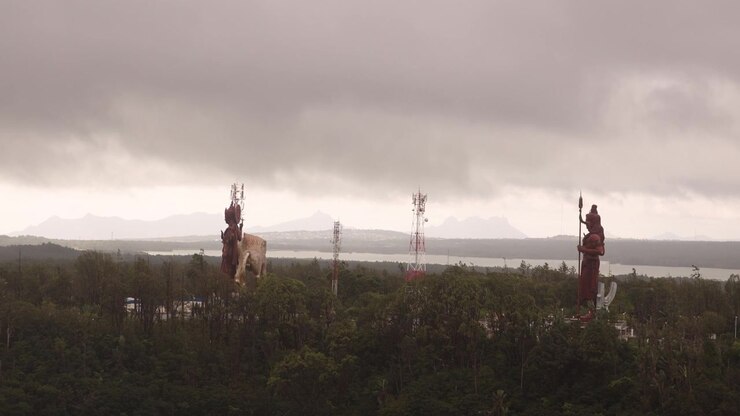 Cloudy aerial view of the sacred Ganga Talao, or Grand Bassin, featuring the colossal Hindu deity statues overlooking the holy crater lake in the mountainous heart of Mauritius.