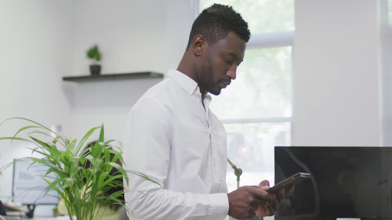 Thoughtful african american businessman using tablet, standing in empty modern office