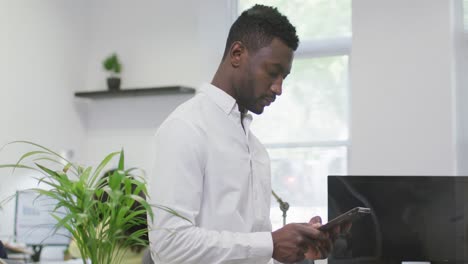 Thoughtful-african-american-businessman-using-tablet,-standing-in-empty-modern-office