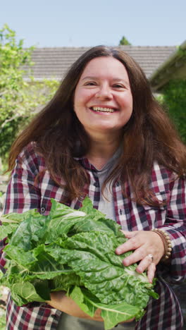 video vertical de una mujer caucásica sonriente en un jardín soleado llevando verduras recién recogidas