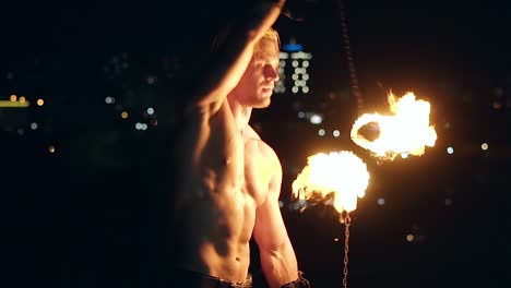 Young-blond-male-spins-two-burning-torches-on-chain-Slow-motion